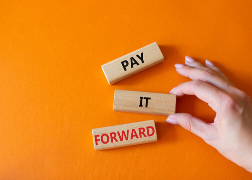 Pay it forward symbol. Concept words Pay it forward on wooden blocks. Beautiful orange background. Businessman hand. Business and Pay it forward concept. Copy space.