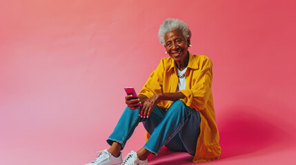 Joyful elderly woman with white hair smiling while using a smartphone, set against a vibrant pink background.