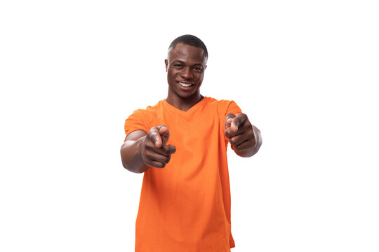 young successful charismatic american man dressed in basic orange t-shirt points with index finger on white background with copy space