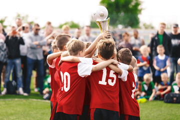 Happy children winning sports tournament. Kids in sports teams win trophies on tournaments Schoolboys standing in a circle and holding the golden trophy. Victory celebration of a youth sports team - obrazy, fototapety, plakaty