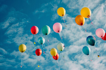 Bunch of colorful helium balloons are floating high up in blue sky. Party and birthday celebration concept