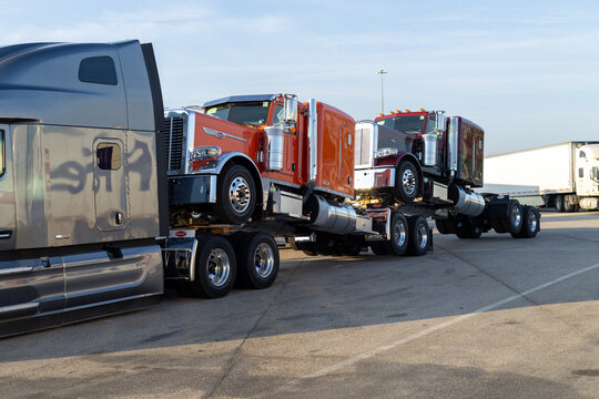 Port Arthur, Texas, USA - 09.11.2023: Semi Trucks Parked in a Row at Truck Stop During Dusk. Red Semi Truck Towed on a Trailer at Truck Stop