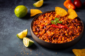 Mexican hot chili con carne in a bowl with tortilla chips on dark background