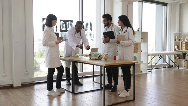 University, education, medicine, anatomy concept. Multiracial medical students with African American professor and human skeleton model in classroom, studying anatomy.