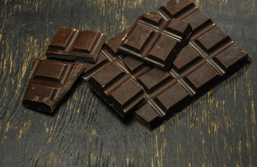pieces of chocolate bar on a dark wooden background. dark photo. broken chocolate bar.