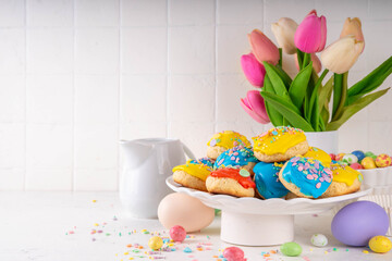 Homemade Italian Easter cookies with colorful sugar glaze and sprinkles, on white kitchen table background, decorated with Easter holiday decor and spring tulip flower bouquet 