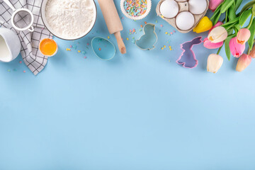 Easter baking background, ingredient for making Easter cookies, cakes, dessert with Easter chocolate eggs, sugar sprinkles, baking ingredients, flour, egg, milk, rolling pin, spring flowers top view - obrazy, fototapety, plakaty