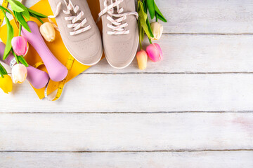 Spring sport fitness background. Outdoors springtime workouts concept. Running sneakers, dumbbell, jump rope, water bottle, tape measure, spring tulip flower, wooden background top view copy space