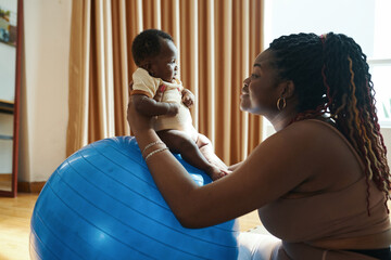 Mother playing with newborn baby, seating her on exercise ball