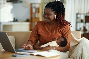 Portrait of smiling Black woman with sleeping baby having online meeting with colleagues