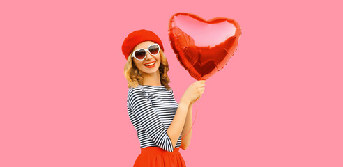 Portrait of happy cheerful smiling woman with red heart shaped balloon wearing french beret on pink background