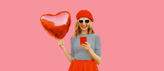 Portrait of pretty happy smiling young woman with mobile phone and red heart shaped balloon wearing...