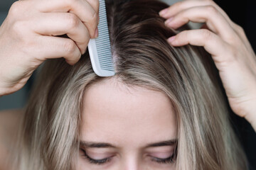 Cropped shot of a young blonde woman parting her hair using a thin comb. Hair styling. Сoloring  the overgrown roots of the head