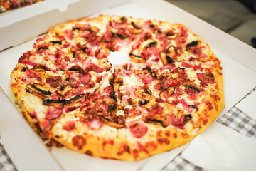 Freshly baked pizza with ham and mushrooms in an open box, cozy indoor setting.