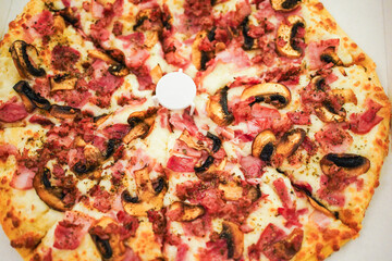 A full pizza with ham and mushrooms, topped with a white pizza saver in the center.