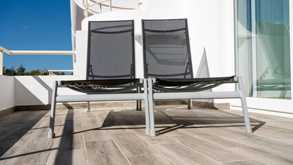 Two green gray sun loungers in the sun and blue sky on a balcony with white walls