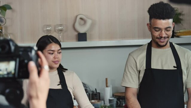 Tilt up shot of chef and his female co-host talking and cooking steak in front of camera while filming culinary show in kitchen