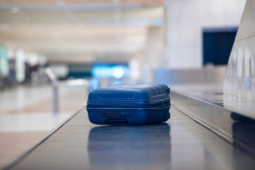 Traveling by airplane. Selective focus on lonely blue suitcase on baggage claim in airport...