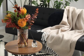 Vase with bouquet of beautiful leucospermum flowers and air freshener on side table near black sofa in room, space for text