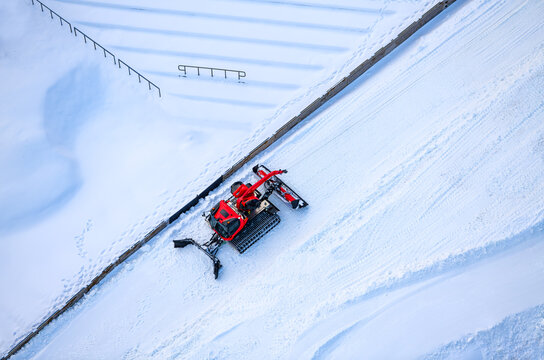 Red snow groomer in bright snowy landscape. Arial view of high tech vehicle preparing snow conditions for ski jumping in “Mühlenkopfschanze“ arena in Willingen, Germany. Seen from suspension bridge.