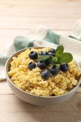 Tasty millet porridge with blueberries and mint in bowl on light wooden table, closeup