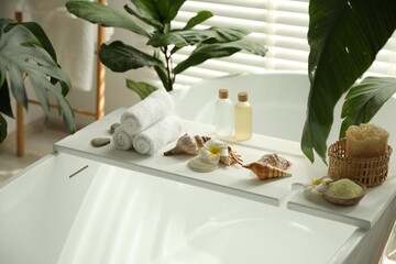 Bath tray with spa products, towels and shells on tub in bathroom