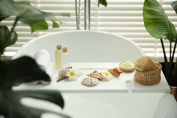 Bath tray with spa products, towels and shells on tub in bathroom
