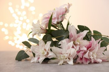 Bouquet of beautiful lily flowers on table against beige background with blurred lights, closeup