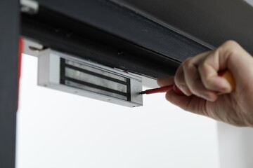 Man with screwdriver installing electromagnetic door lock indoors, closeup. Home security