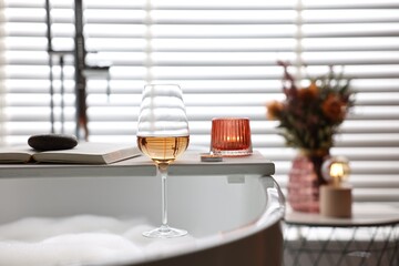 White wooden tray with glass of rose wine, book and burning candles on bathtub in bathroom