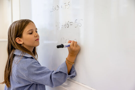 Little girl counting math equation on whiteboard in school.