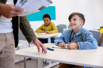 Unrecognizable male teacher giving tasks on paper to pupils in classroom.