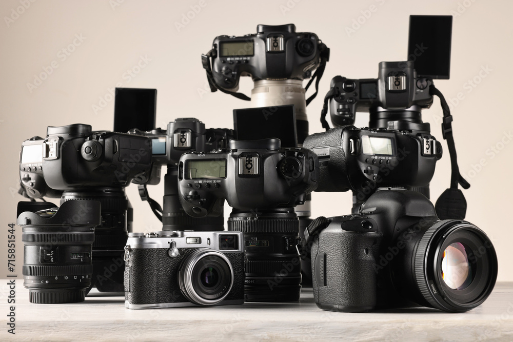 Poster Modern cameras on white wooden table against light background