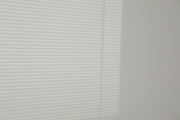 Light and shadow from window shutters on white wall, space for text