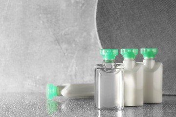 Mini bottles of cosmetic products on grey textured table, space for text