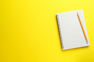 Notebook and pencil on yellow background, top view. Space for text