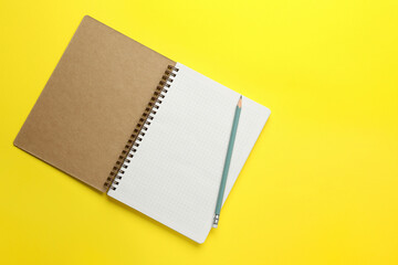 Notebook and pencil on yellow background, top view. Space for text