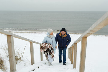 An elderly couple climbs a wooden staircase in winter by the sea