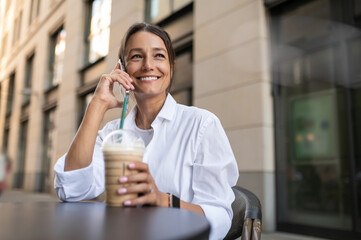 Dark-haired woman having coffee and holding a phone in hand