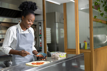 Smiling dark-skinned woman preparing pizza and looking contented