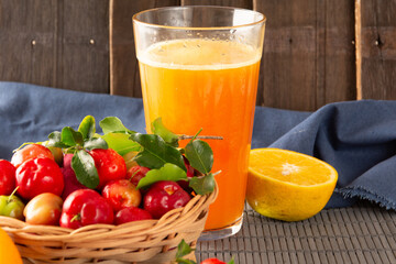 Fresh acerola juice in a glass cup in a bamboo place mat with sliced oranges and acerola fruits front view