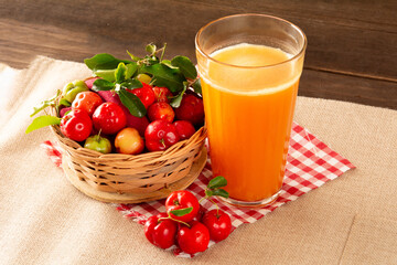 Fresh acerola juice in a glass cup in a bamboo place mat with sliced oranges and acerola fruits front view