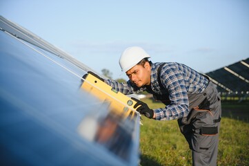 An Indian worker in uniform and with tools works on a solar panel farm