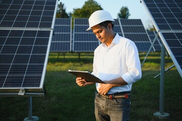 An Indian male engineer working on a field of solar panels. The concept of renewable energy