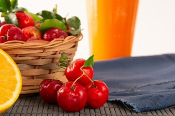 Fresh acerola juice in a glass cup in a bamboo place mat with sliced oranges and acerola fruits front view