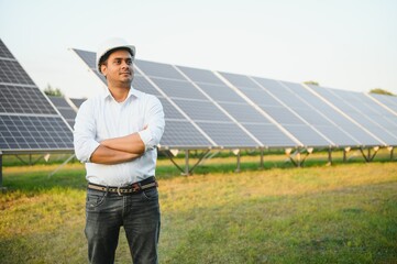 An Indian male engineer working on a field of solar panels. The concept of renewable energy