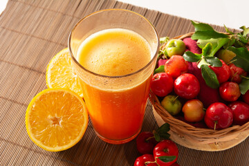 Fresh acerola juice in a glass cup in a bamboo place mat with sliced oranges and acerola fruits top view