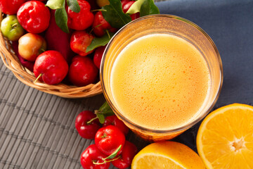 Fresh acerola juice in a glass cup in a bamboo place mat with sliced oranges and acerola fruits top view