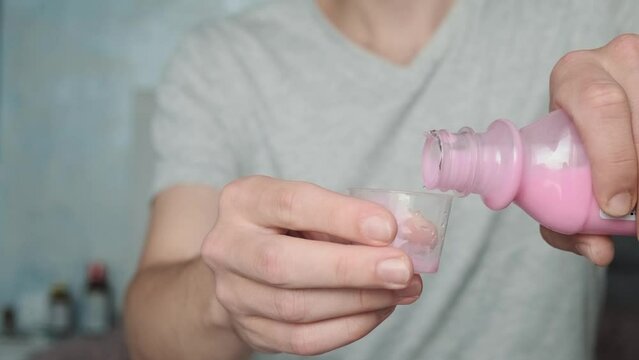 Man drinking antacid syrup to treat gastritis, stomach ulcer, heartburn, acid indigestion from measuring cup. Taking medicine, health care, pharmacy and treatment concept. Selective focus