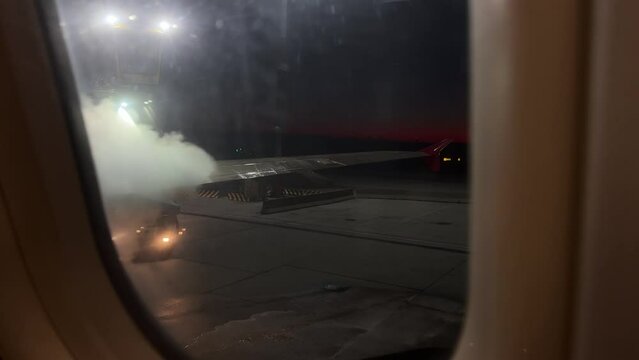 View from airplane window of the wing being sprayed with deicing fluid in darkness